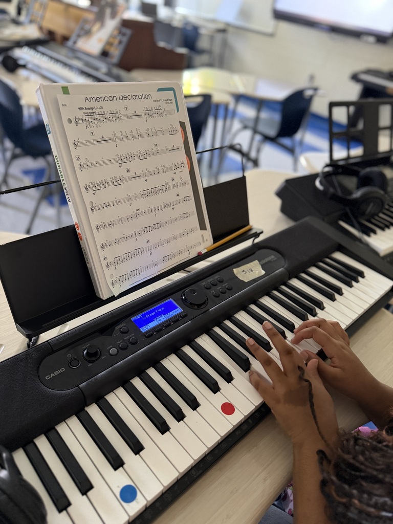 A piano keyboard with sheet music above it and a students hands on the keys is shown.