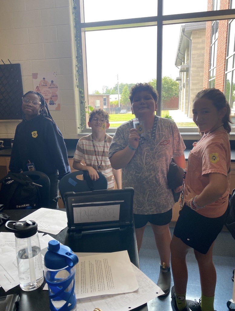 A group of four 6th grade science students pose for the camera showing their detective stickers they received after their science lab investigation.
