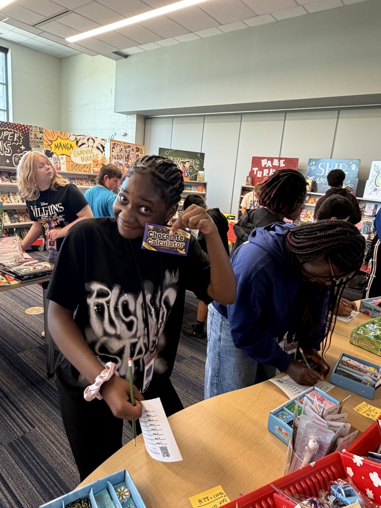 A female student holds up a chocolate scented calculator and looks at the camera smiling while shopping the book fair.