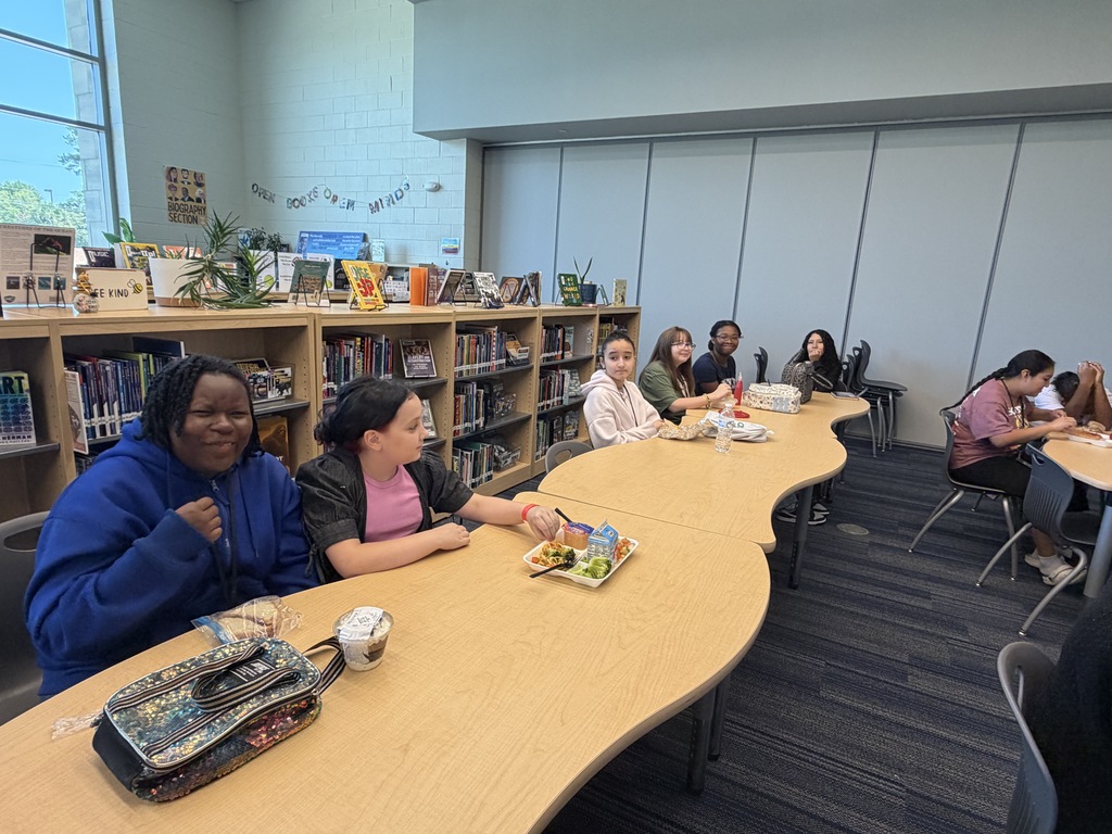 Students gathered in the library sitting at tables while eating lunch and participating in the Fulmer library and public library collaboration event.