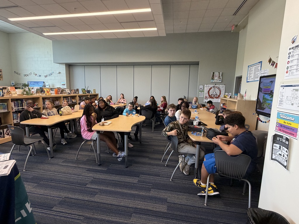 Students gathered in the library sitting at tables while eating lunch and participating in the Fulmer library and public library collaboration event.