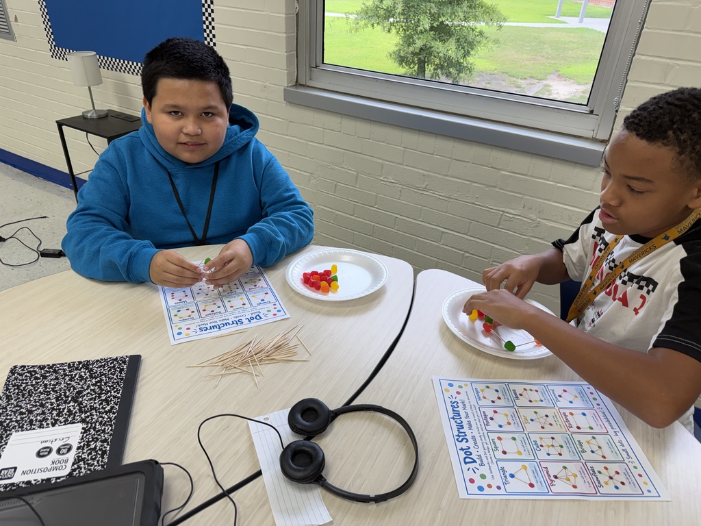 Two students are sitting at their desks putting together their dot structures using toothpicks and DOT gummy candy.
