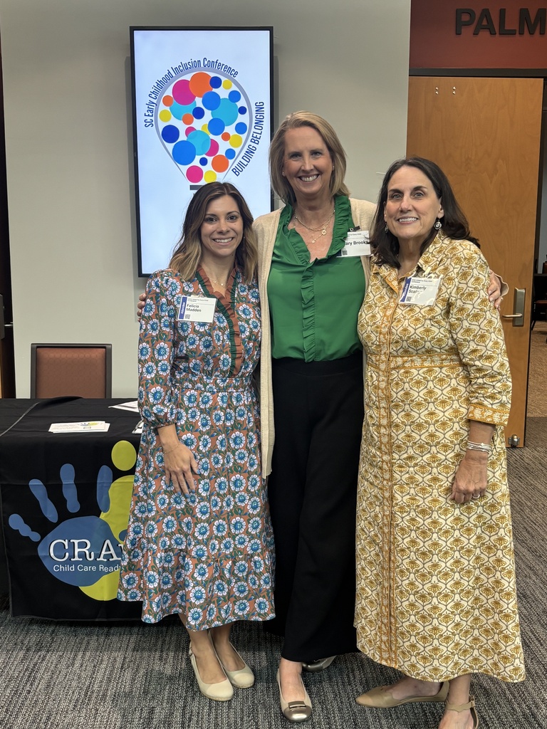Three ladies dressed professionally standing in front of a light bulb shaped sign for a preschool inclusion conference