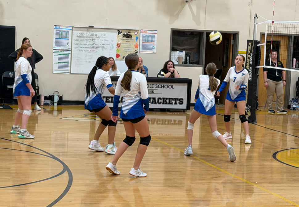 Fulmer volleyball girls are standing on the court watching the ball as one of the top row players is going to volley the ball.