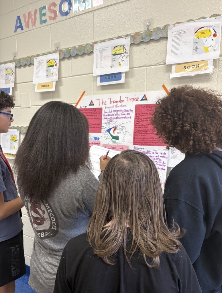 7th grade social studies students are conducting a gallery walk by viewing different student group posters that share information about West African culture as they wrapped up this unit in class. Students are shown walking around with a paper and pencil in hand as they look at the different posters taped on the wall in different places in the classroom.