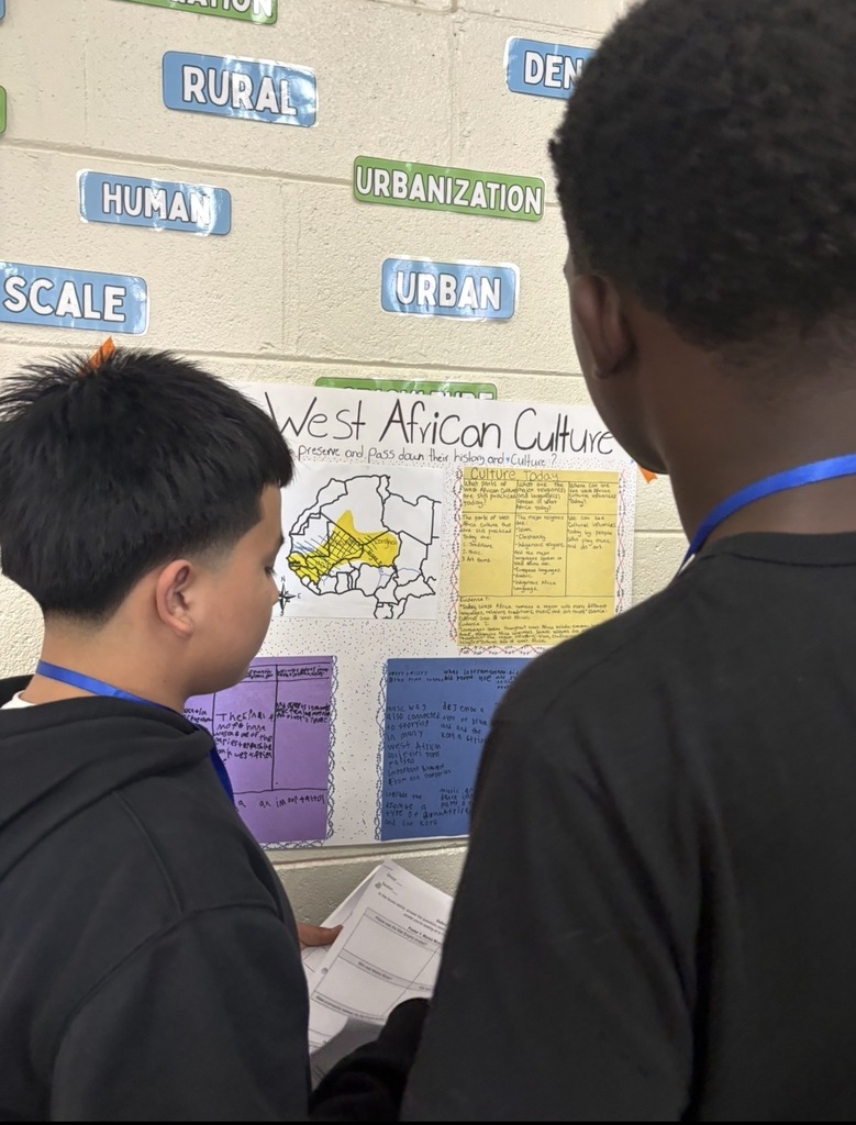 7th grade social studies students are conducting a gallery walk by viewing different student group posters that share information about West African culture as they wrapped up this unit in class. Students are shown walking around with a paper and pencil in hand as they look at the different posters taped on the wall in different places in the classroom.