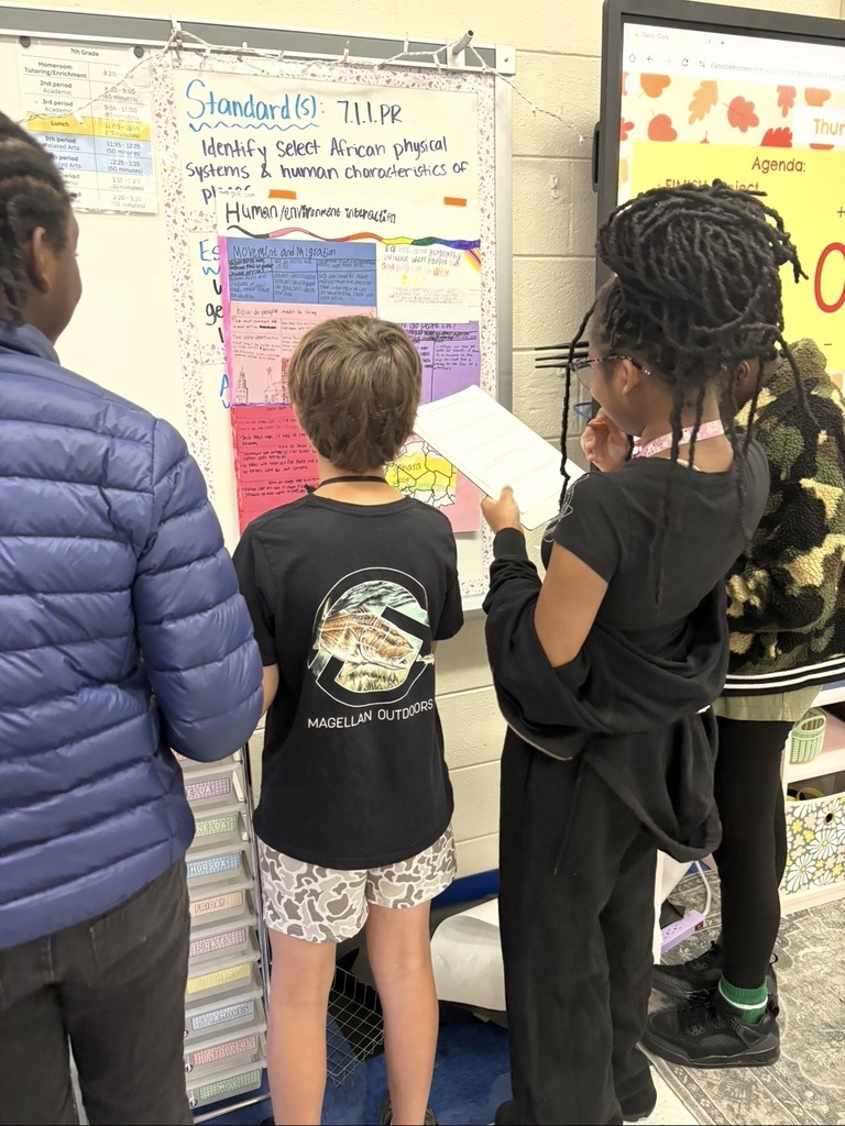 7th grade social studies students are conducting a gallery walk by viewing different student group posters that share information about West African culture as they wrapped up this unit in class. Students are shown walking around with a paper and pencil in hand as they look at the different posters taped on the wall in different places in the classroom.
