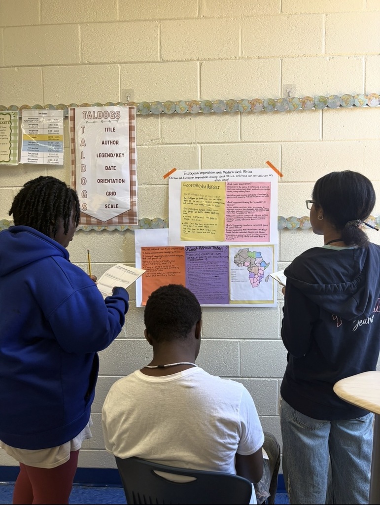 7th grade social studies students are conducting a gallery walk by viewing different student group posters that share information about West African culture as they wrapped up this unit in class. Students are shown walking around with a paper and pencil in hand as they look at the different posters taped on the wall in different places in the classroom.