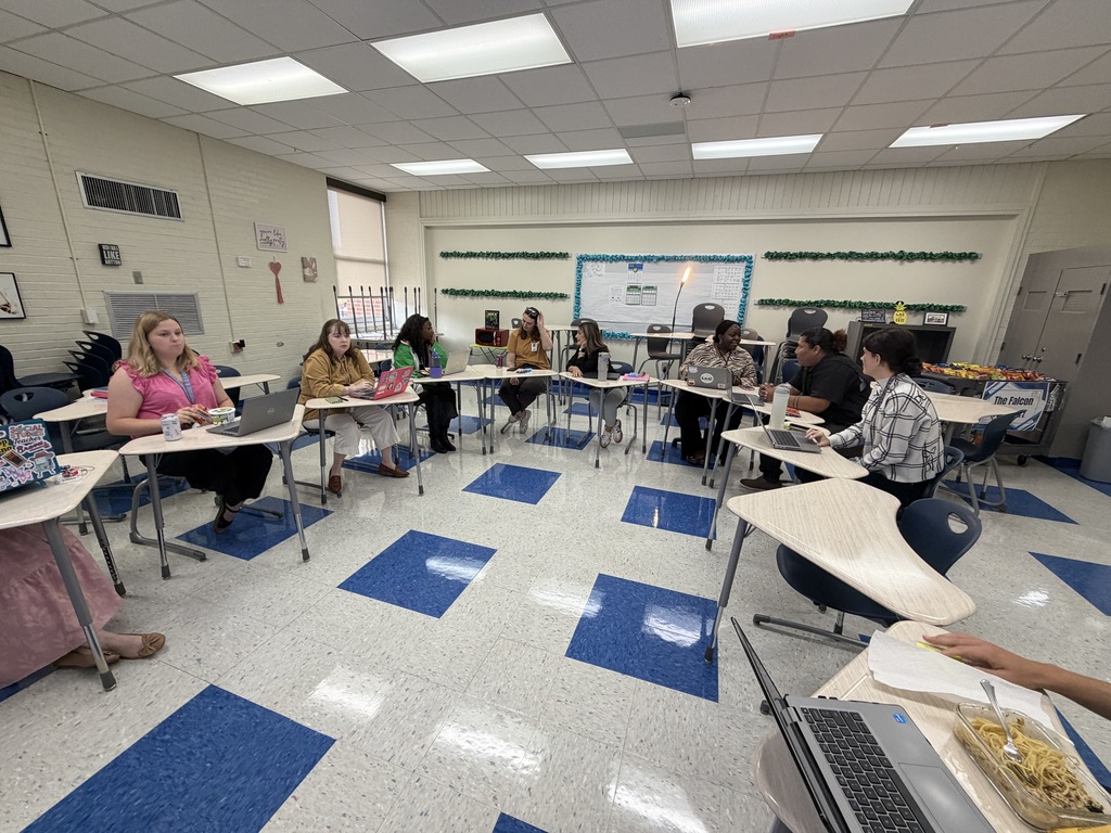 The 7th grade team, Dr. Johnson, and the two school counselors are shown seated in a half circle in student desks for a team meeting.