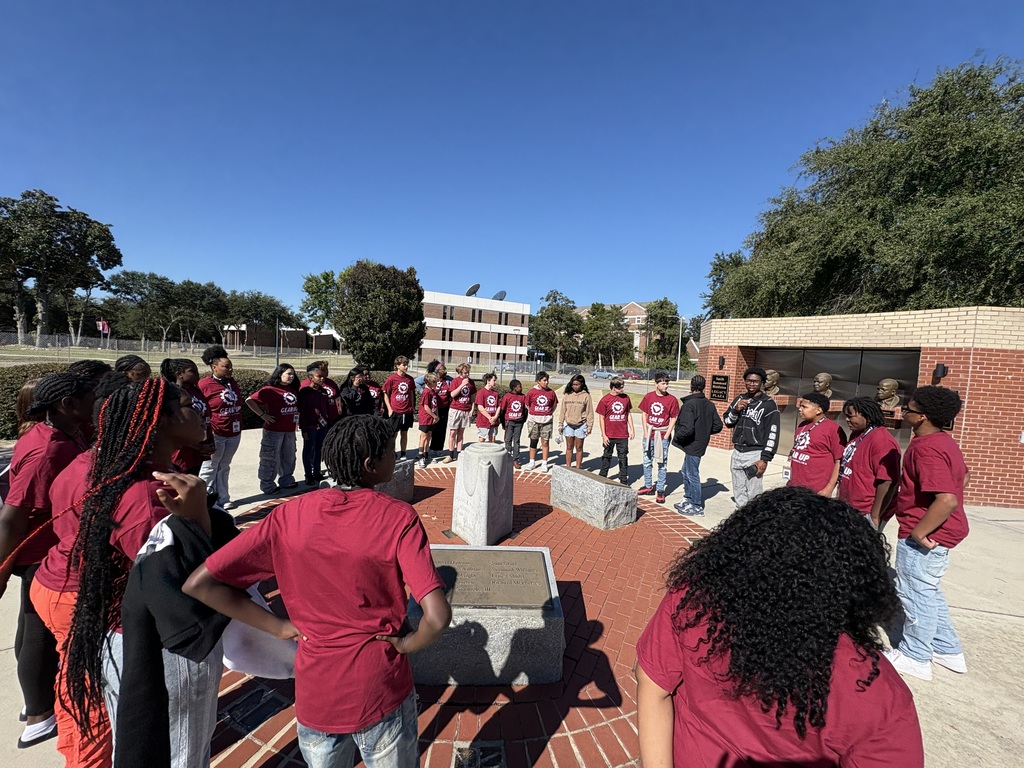 A group of male and female students are standing outside listening to one of the adult tour guides.