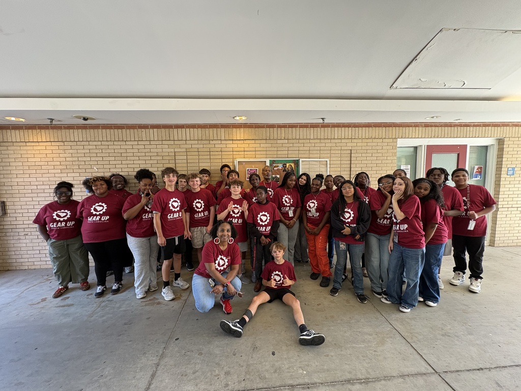 A group of male and female students along with the adult mentor advisors and a college employee/student are standing for a group photo on site at the college.