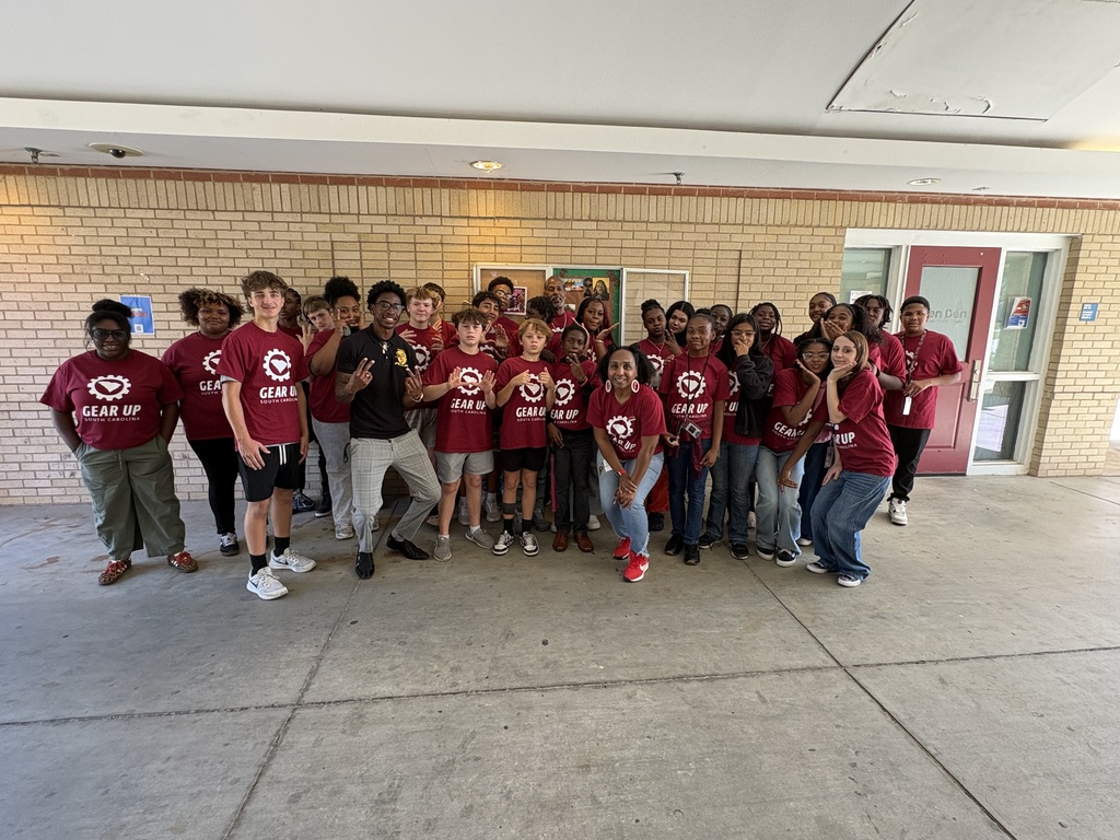 A group of male and female students along with the adult mentor advisors and a college employee/student are standing for a group photo on site at the college.