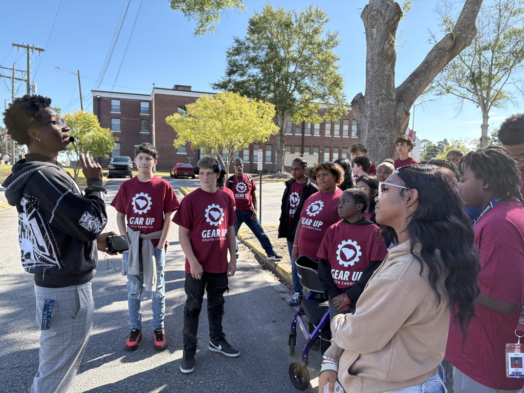 A group of male and female students are standing outside listening to one of the adult tour guides.