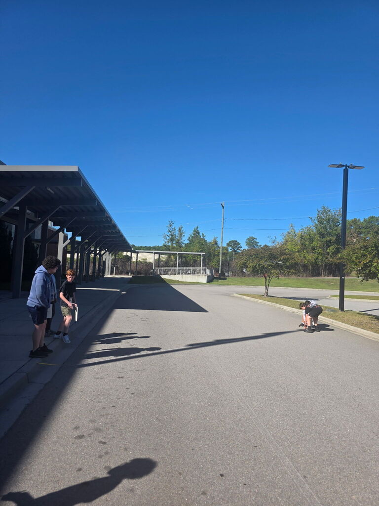 Three students are shown outside measuring the flagpole's shadow.