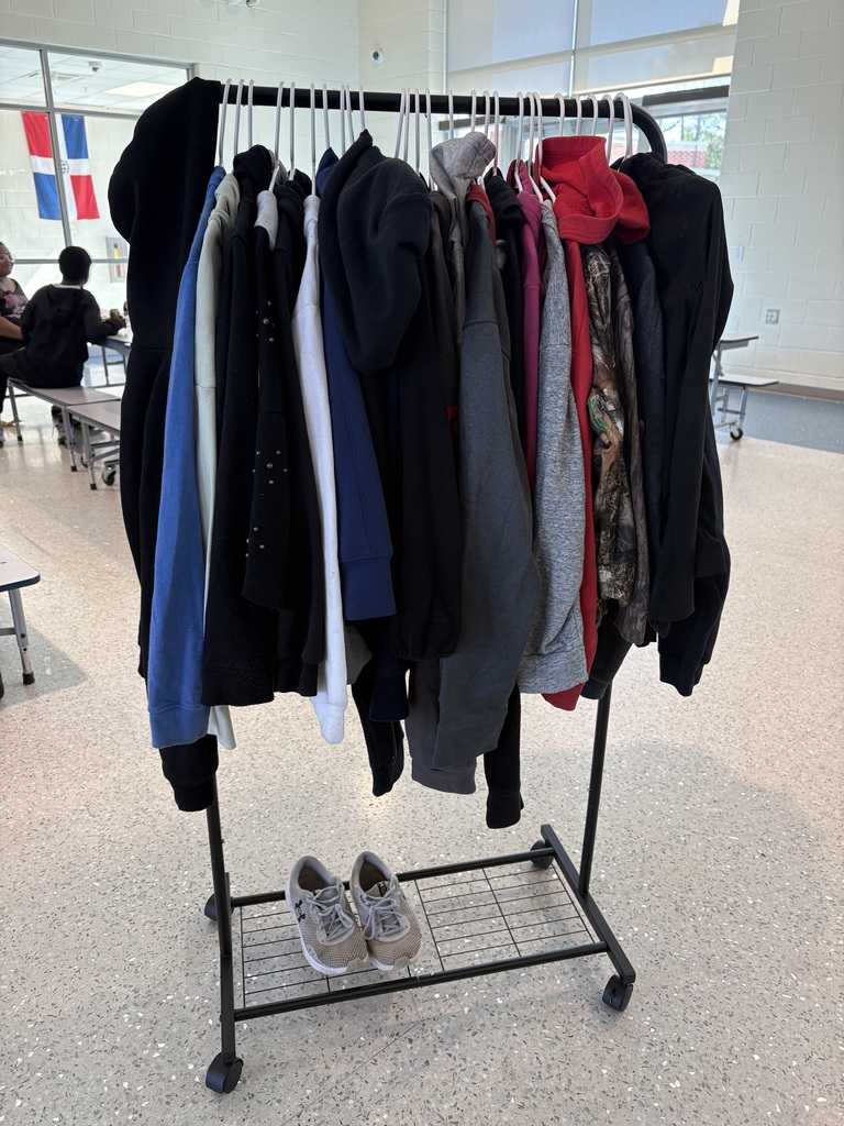 Coats and hoodies are shown hanging on a black cart rack in the cafeteria. There's a pair of Under Armour tennis shoes on the bottom of the rack.