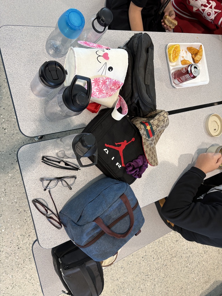 There are several different items such as water bottles, lunch boxes, and glasses shown scattered on two cafeteria tables.