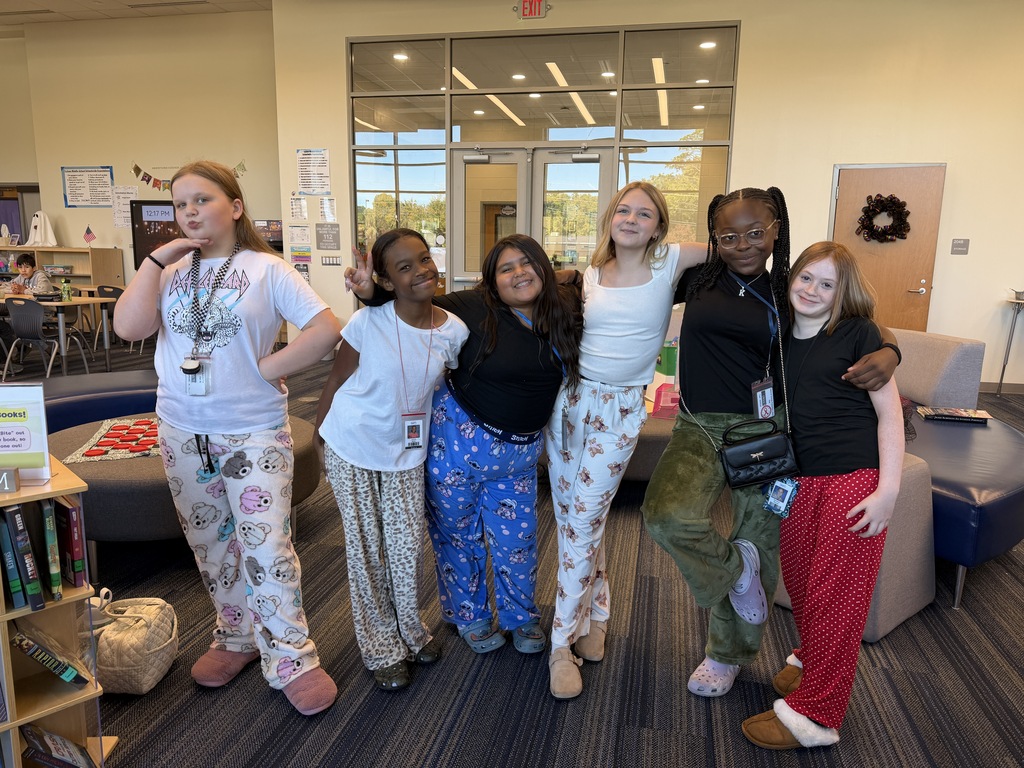 A group of female students are standing in the library with arms wrapped around each other smiling at the camera wearing pajama pants.