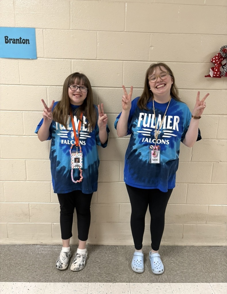 A student and a teacher stand side by side smiling at the camera wearing the exact clothing attire for Twin Day at school. They are both holding up both of their hands in the peace sign symbol.