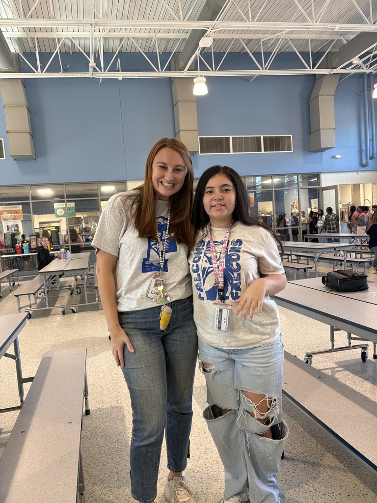 Two people, a teacher and a student, stand side by side smiling at the camera wearing the exact clothing attire for Twin Day at school. 