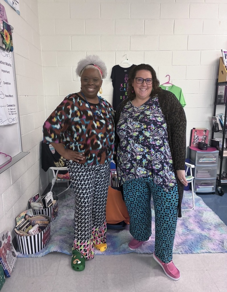 Two faculty member stand side by side smiling at the camera wearing mismatched clothing and shoes.