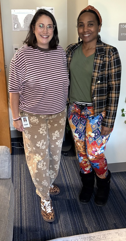 Two faculty member stand side by side smiling at the camera wearing mismatched clothing and shoes.