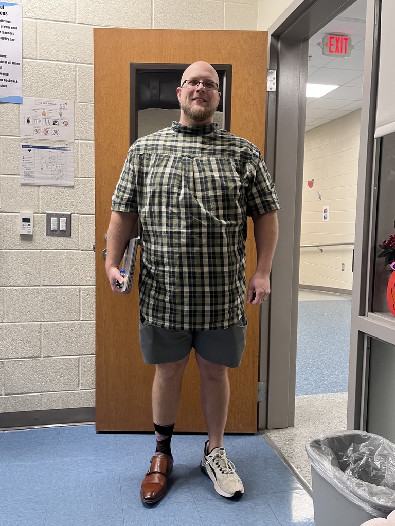 One teacher stands smiling at the camera wearing mismatched clothing and shoes.