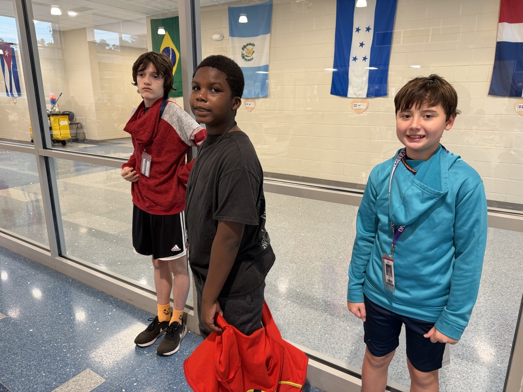 Three students stand side by side wearing backwards clothing. The two boys on the right are looking and smiling at the camera while the other boy on the left is looking off somewhere else.