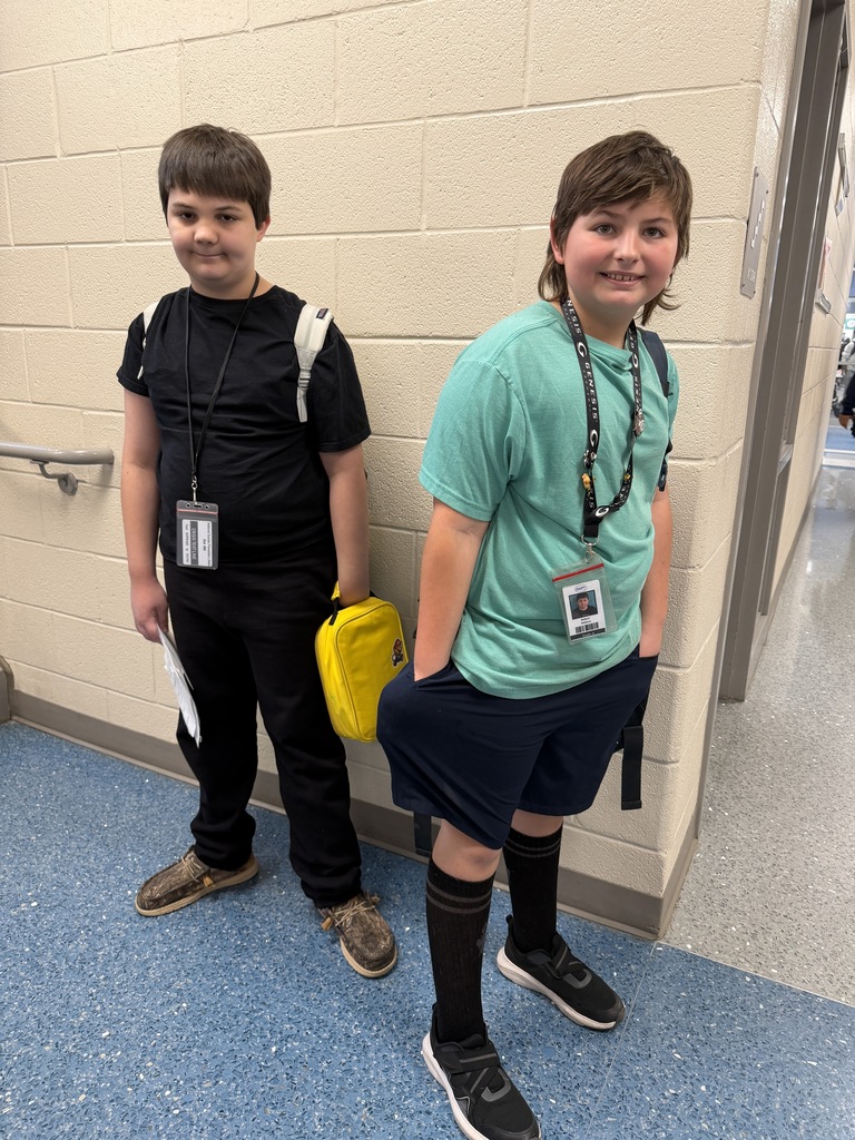 Two students smile and stand together in the hallway wearing backwards clothing.