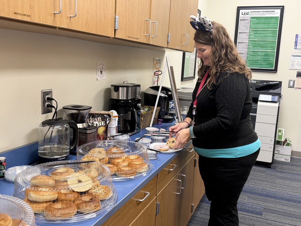 Ms. Alfrey is putting cream cheese on her bagel at the bagel bar.