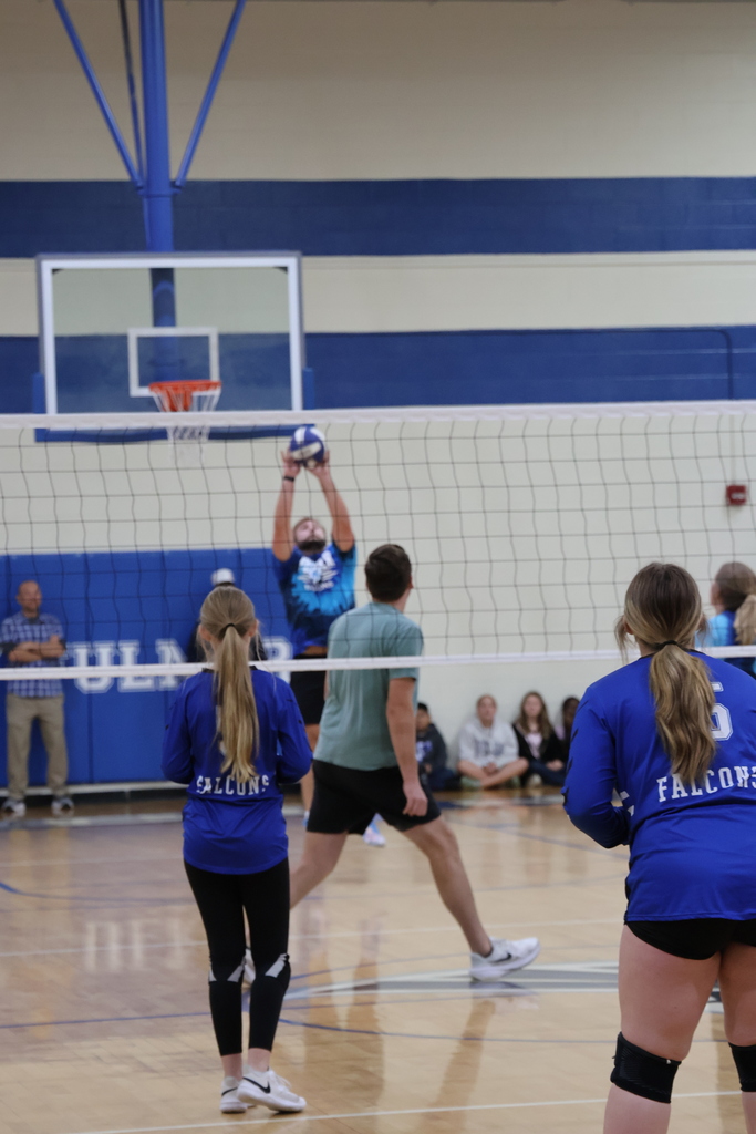 Mr. Payne is shown reaching up high to volley the ball back across the net two the volleyball team with two girls on the team facing towards their opponent.