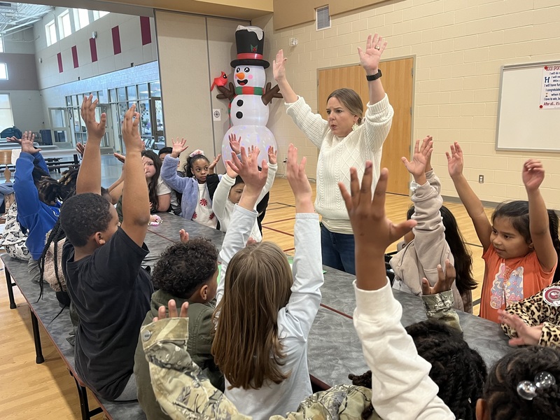 Jennifer Cribbs, coordinator of Science, and students raise their arms high to show that snow starts way up in the clouds