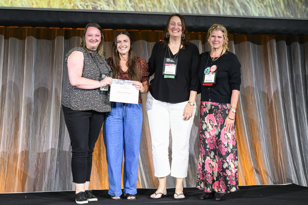 Four women smiling on a stage holding a certificate