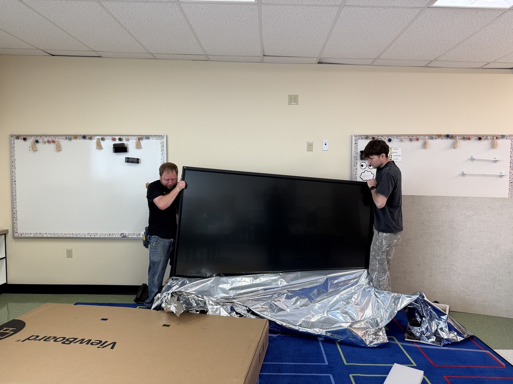 Two men hanging a big screen in a classroom