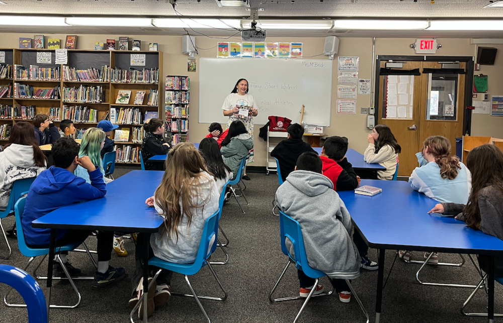 Students at tables in the library listen to a speaker