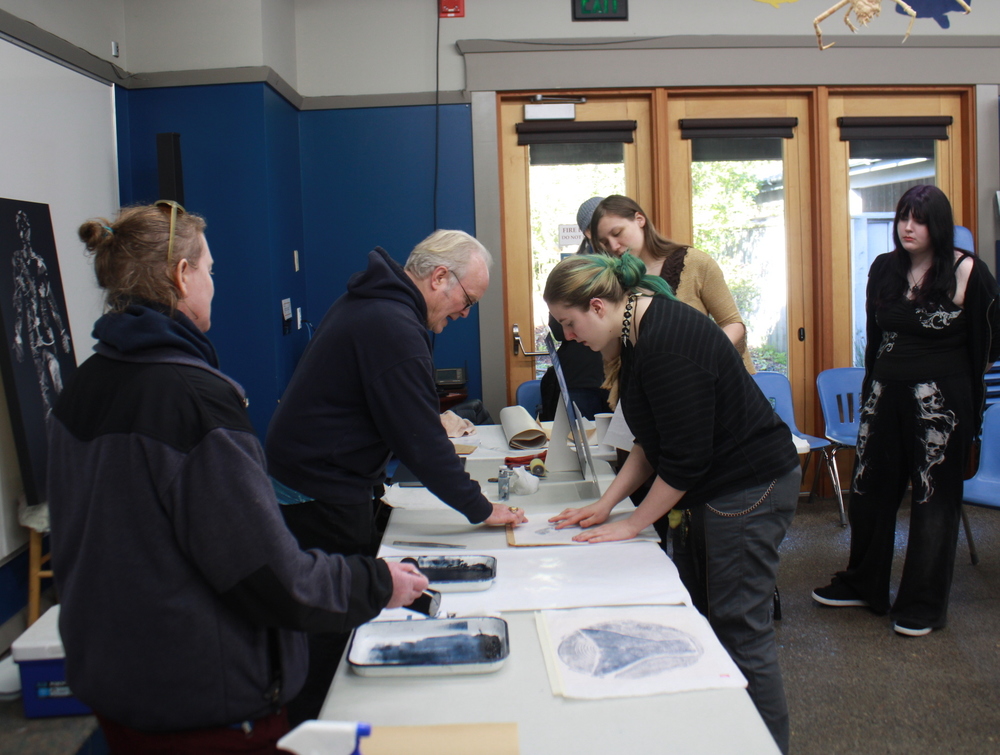 Students standing at a table pressing on paper
