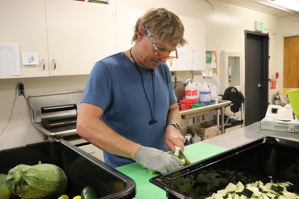 Blond man in blue tshirt chopping squash on a green cutting board