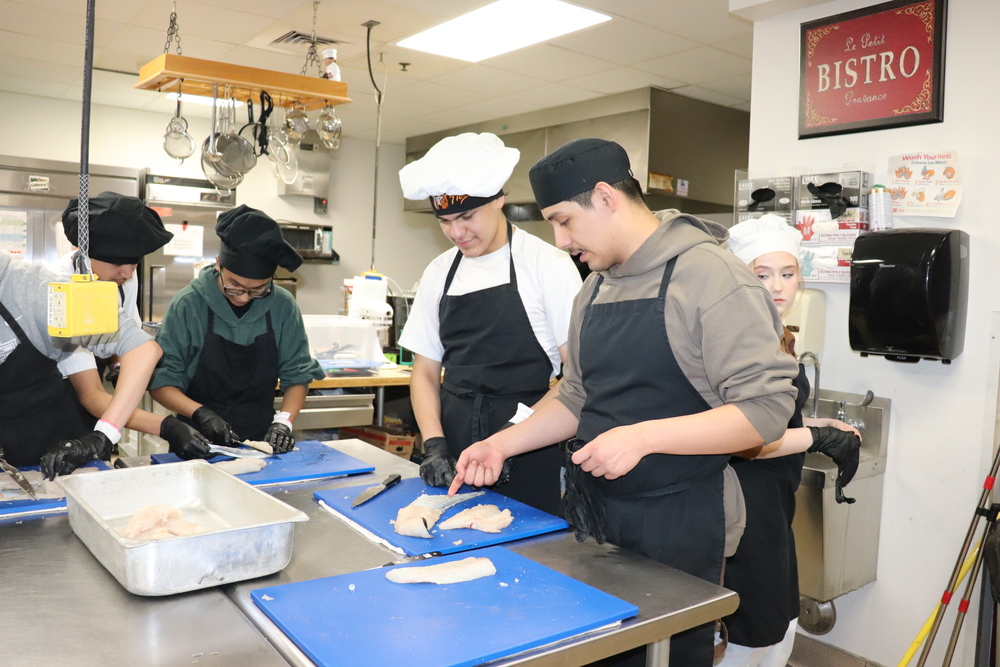 Culinary students in a kitchen butchering fish filets