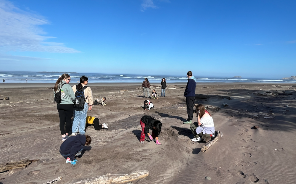 students digs in sand on the beach as older students supervise