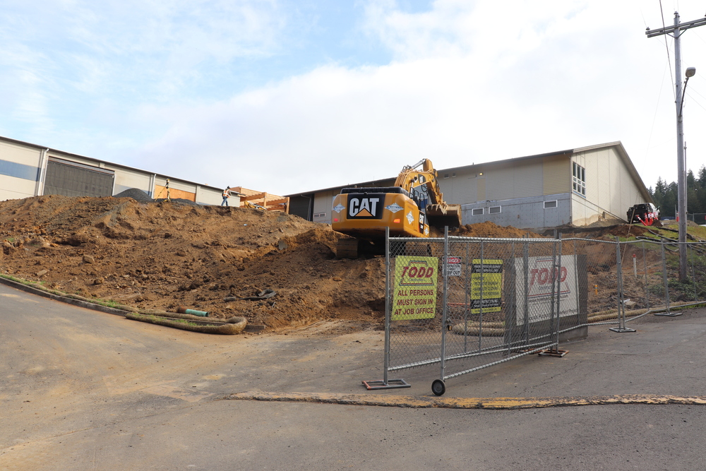 Backhoe on a big mound of dirt in front of a school