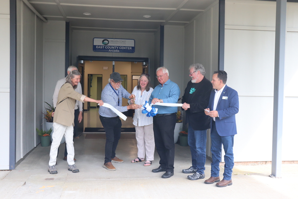 7 middle aged people cutting a ribbon in front of a door