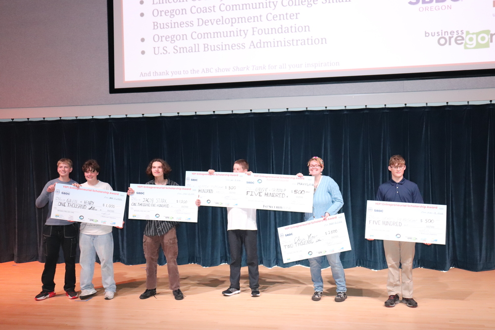 Six sstudents stand while holding large checks