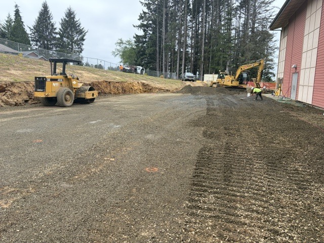 2 heavy equipment machines leveling ground near a school