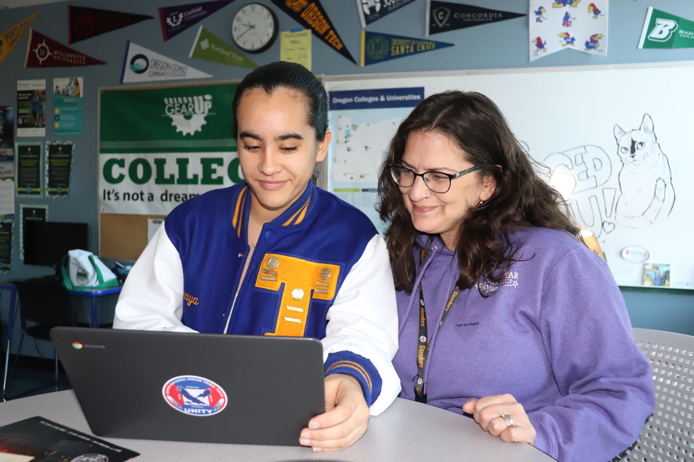 Student in letter jacket and woman in purple sweatshirt look at a laptop