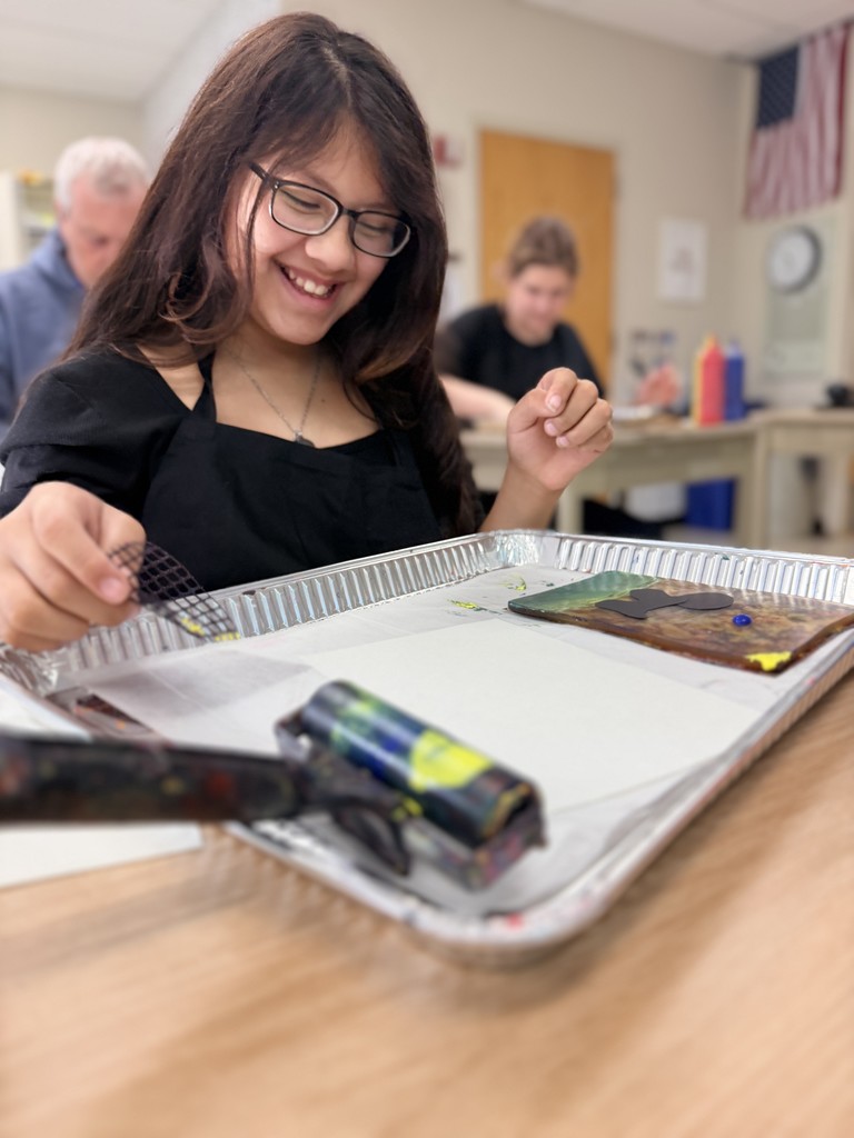 Here a student prepares for the art project of monotype prints. There is a roller and a Gelli plate ready for art to be created.