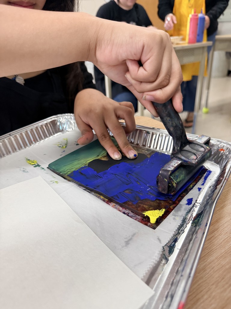 The student uses a roller to press paint onto their paper.