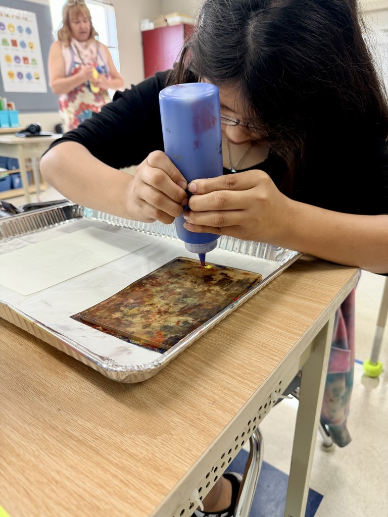 In this image, a student uses a paint bottle to apply paint to the Gelli plate.