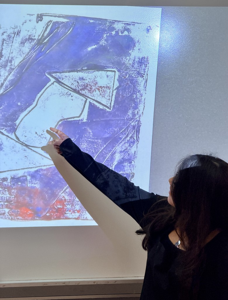 Student walks her audience through her art creation, which is full of deep purple colors and a hint of some red. The student has an geometric shaped object in the center of her work.