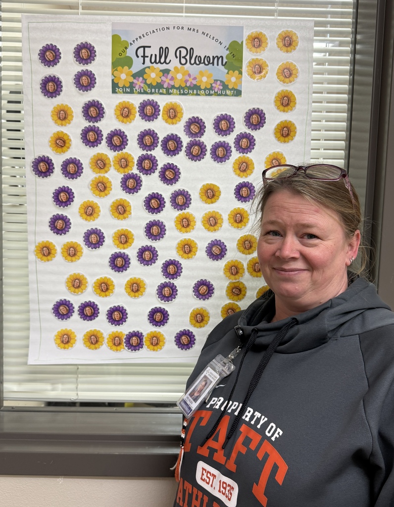 Mrs Nelson smiling beside a poster filled with flower stickers.  Sra Nelson de pie junto a un póster lleno de pegatinas de flores.