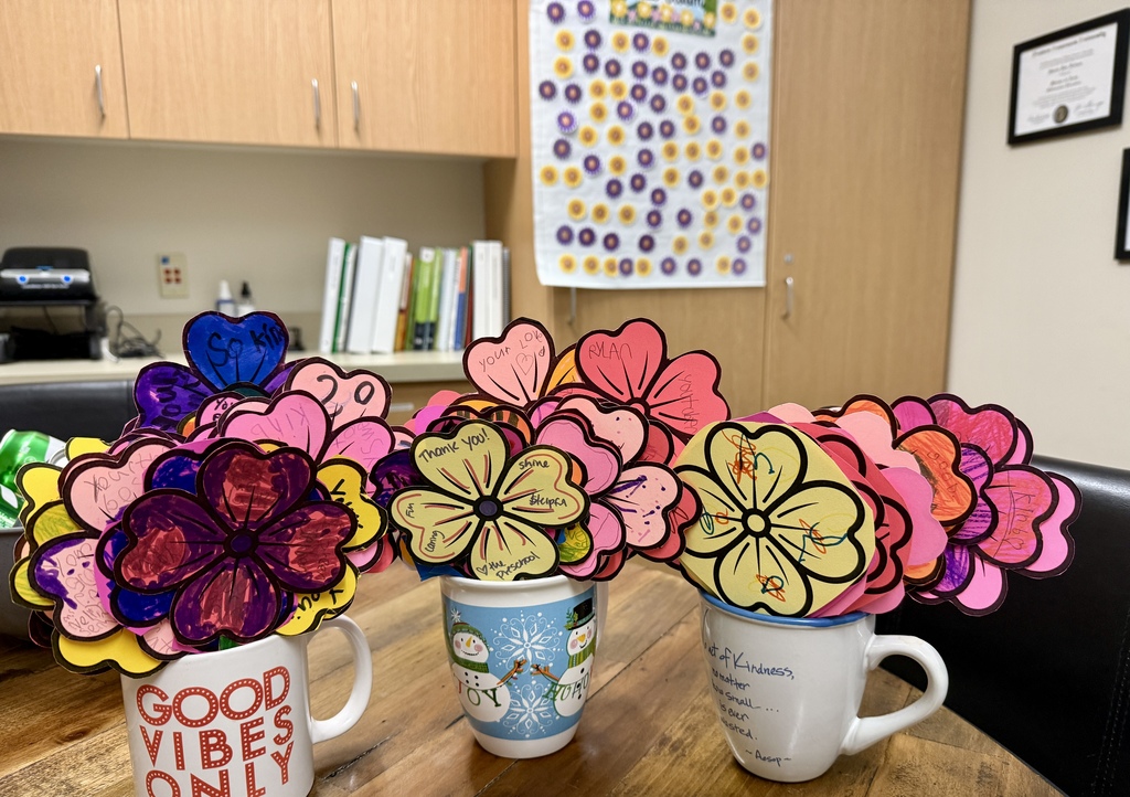 Colorful paper flowers with handwritten notes arranged in mugs on a table.  Flores de papel coloridas con mensajes escritos a mano colocadas en tazas sobre una mesa.