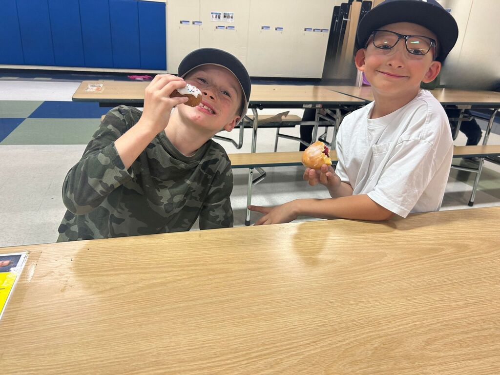 Smiling boys holding donuts in school cafeteria.